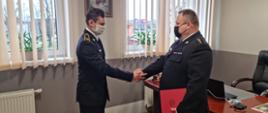 Fotografia przedstawia Komendanta Powiatowego PSP w Malborku w trakcie wręczania nominacji. Funkcjonariusze ubrani są w mundury wyjściowe koloru granatowego. 