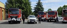 samochody strażackie stojące na placu przed garażami, obok dwóch stoją strażacy