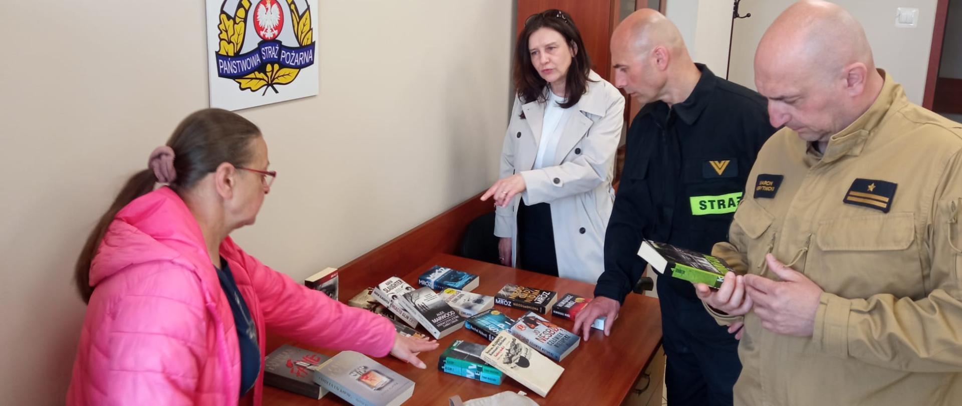  Fotografia przedstawia funkcjonariuszy i panie bibliotekarki, które przybliżają tematykę przyniesionych książek.