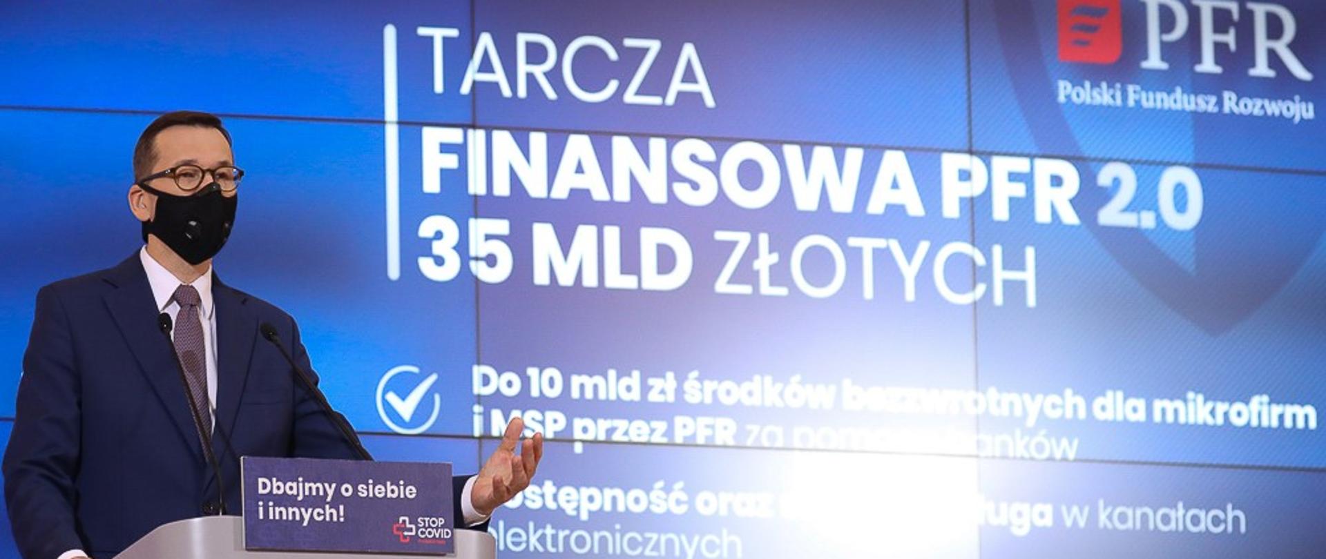 Premier Mateusz Morawiecki stoi przy mównicy, w tle prezentacja.