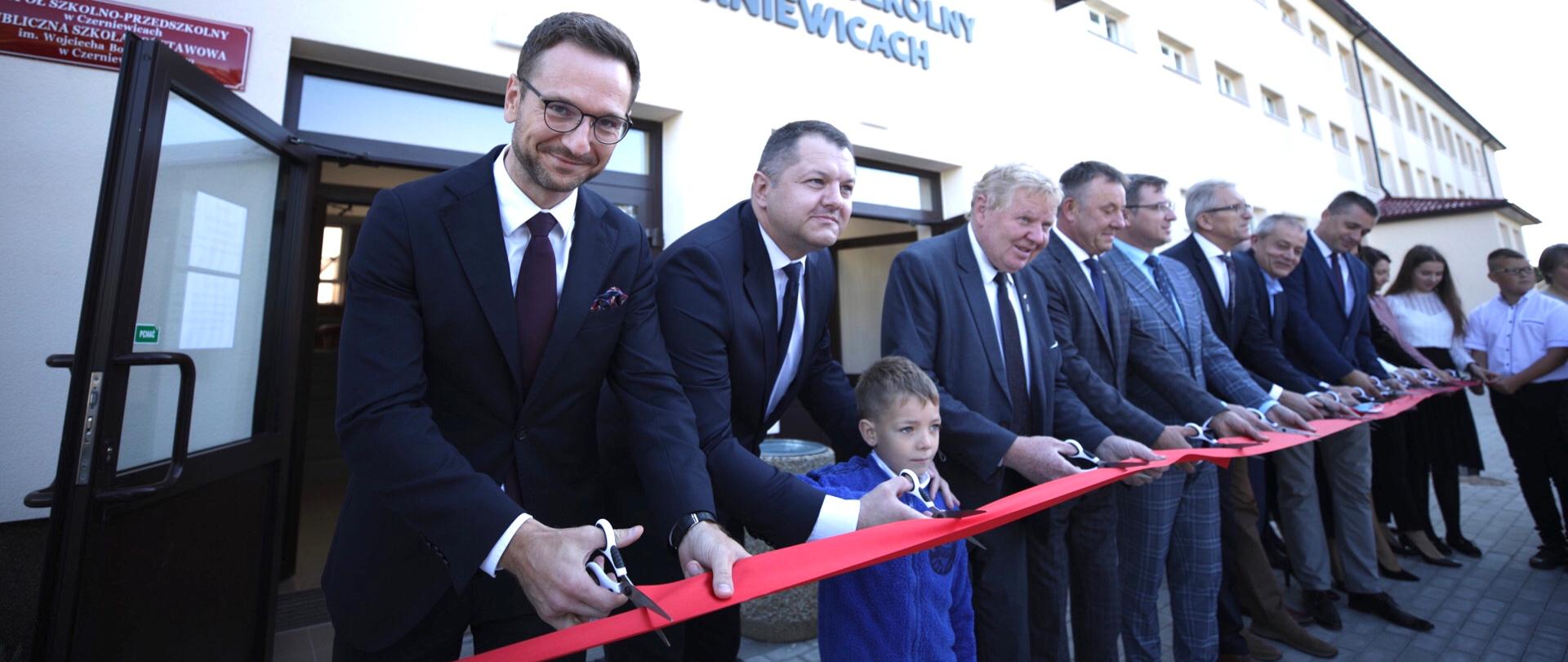 Minister Waldemar Buda przecina czerwoną wstęgę jako symbol oficjalnego otwarcia Zespołu Szkolno-Przedszkolnego w Czerniewicach