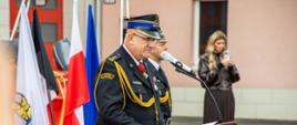 Fotografia przedstawia oficjalne wystąpienie Komendanta Powiatowego PSP w Lubinie podczas uroczystych obchodów Dnia Strażaka na otwartej przestrzeni.