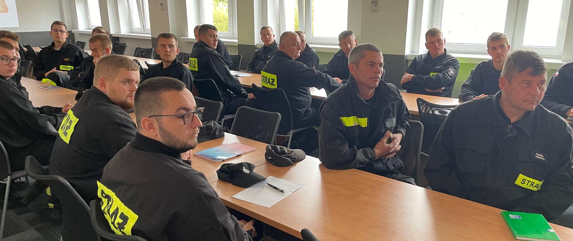 Na zdjęciu widzimy słuchaczy kursu, strażaków OSP, siedzących w sali wykładowej. Strażacy w czarnych mundurach OSP.