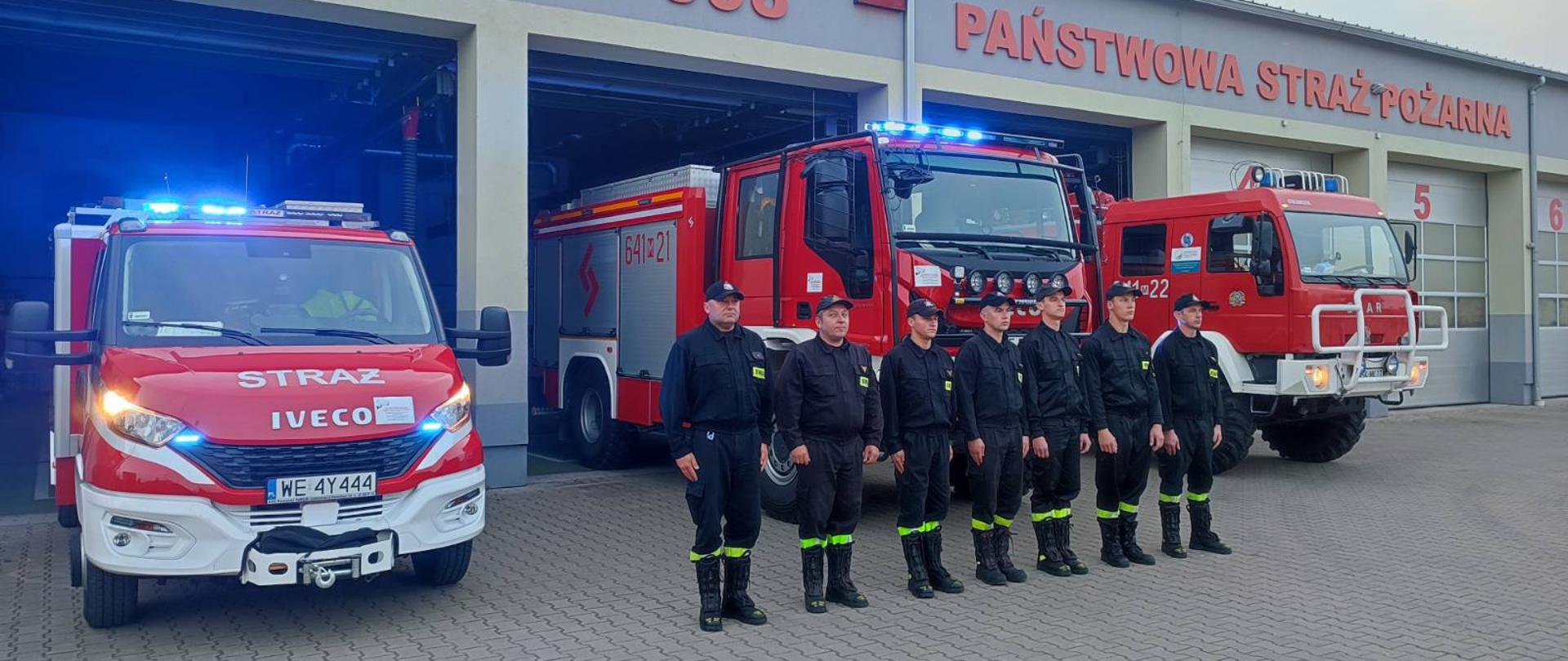 Minuta ciszy dla druha z OSP Balice - na zdjęciu strażacy w ubraniu koszarowym na placu przed strażnicą na zbiórce w szeregu przed czerwonymi samochodami strażackimi.
