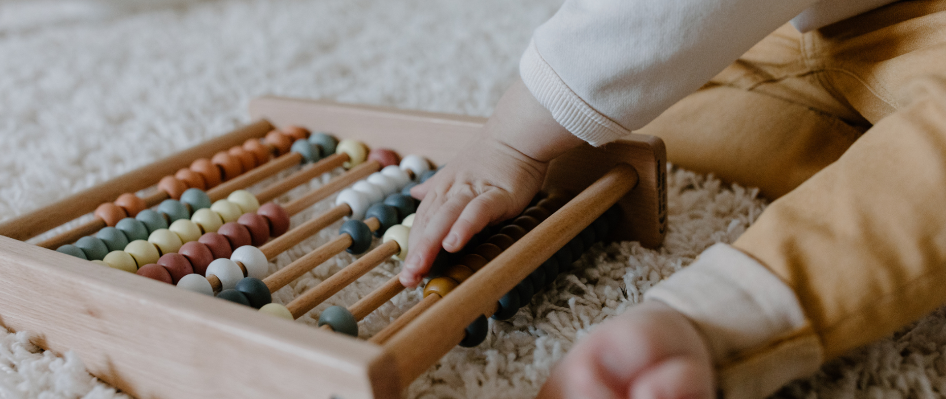 na dywanie siedzi malutkie dziecko i bawi się liczydłem