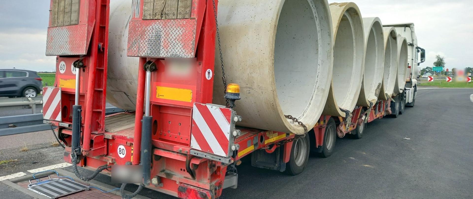 Na pierwszym planie zestaw ciężarowy z pięcioma dużymi rurami betonowymi. Ciężarówką stoi tuż za przenośnymi wagami ITD.