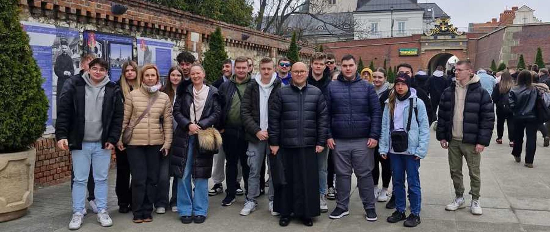 To zdjęcie przedstawia grupę osób odwiedzających Jasną Górę w Częstochowie. Oto kilka kluczowych informacji o tym miejscu:
Znaczenie: Jasna Góra to jedno z najważniejszych miejsc kultu maryjnego w Polsce oraz kluczowe centrum pielgrzymkowe katolików.
Lokalizacja: Sanktuarium wraz z klasztorem zakonu paulinów położone jest na wzgórzu o tej samej nazwie w Częstochowie.
Obraz: W klasztorze znajduje się cudowny obraz Matki Bożej Częstochowskiej, który przyciąga rzesze pielgrzymów z całego kraju i świata.
Historia i sztuka: Obiekt gromadzi liczne dzieła sztuki sakralnej, w tym dary wotywne wiernych składane przez stulecia.
Turystyka: Oprócz funkcji religijnych, Jasna Góra jest ważnym punktem na mapie turystycznej, oferując zwiedzającym m.in. bazylikę, kaplicę Matki Bożej oraz liczne muzea i wystawy.