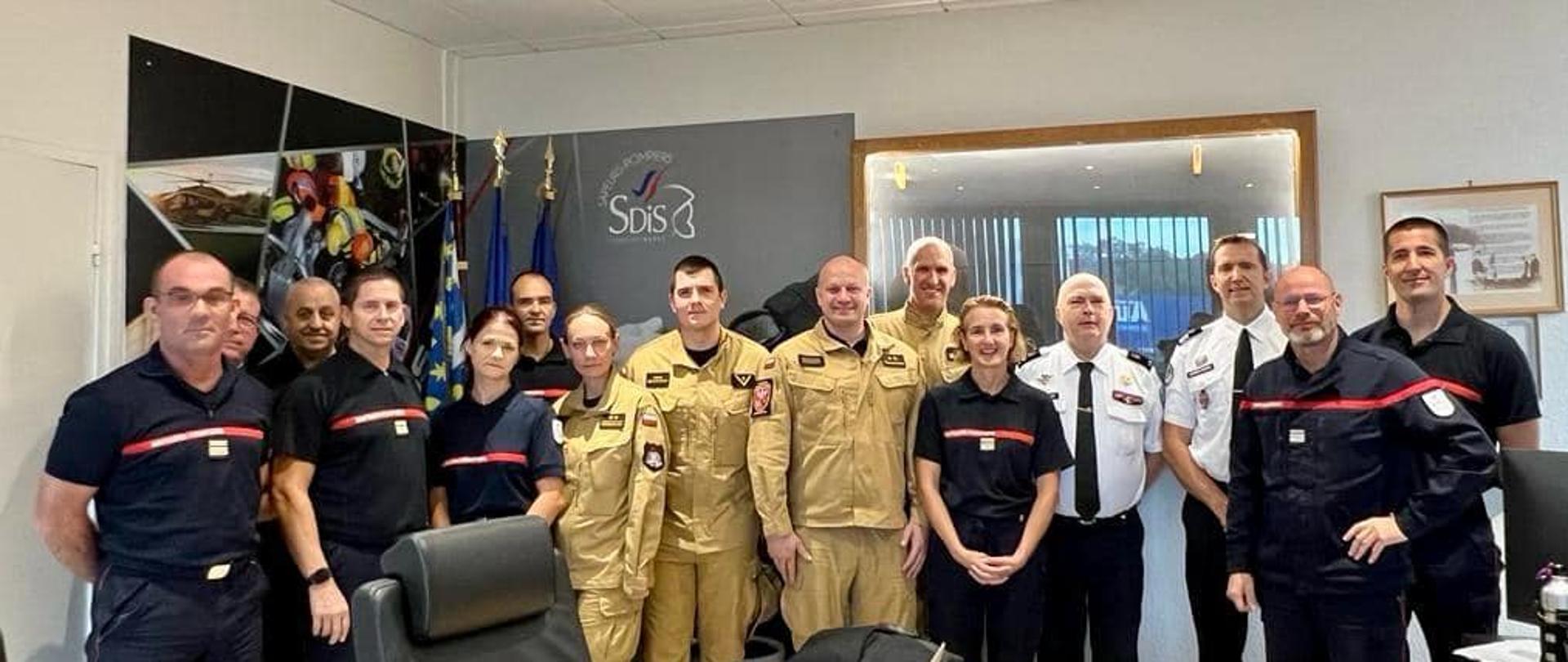 Grupa strażaków polskich i francuskich w mundurach stoi w biurze , na drzwiach napis SDiS
