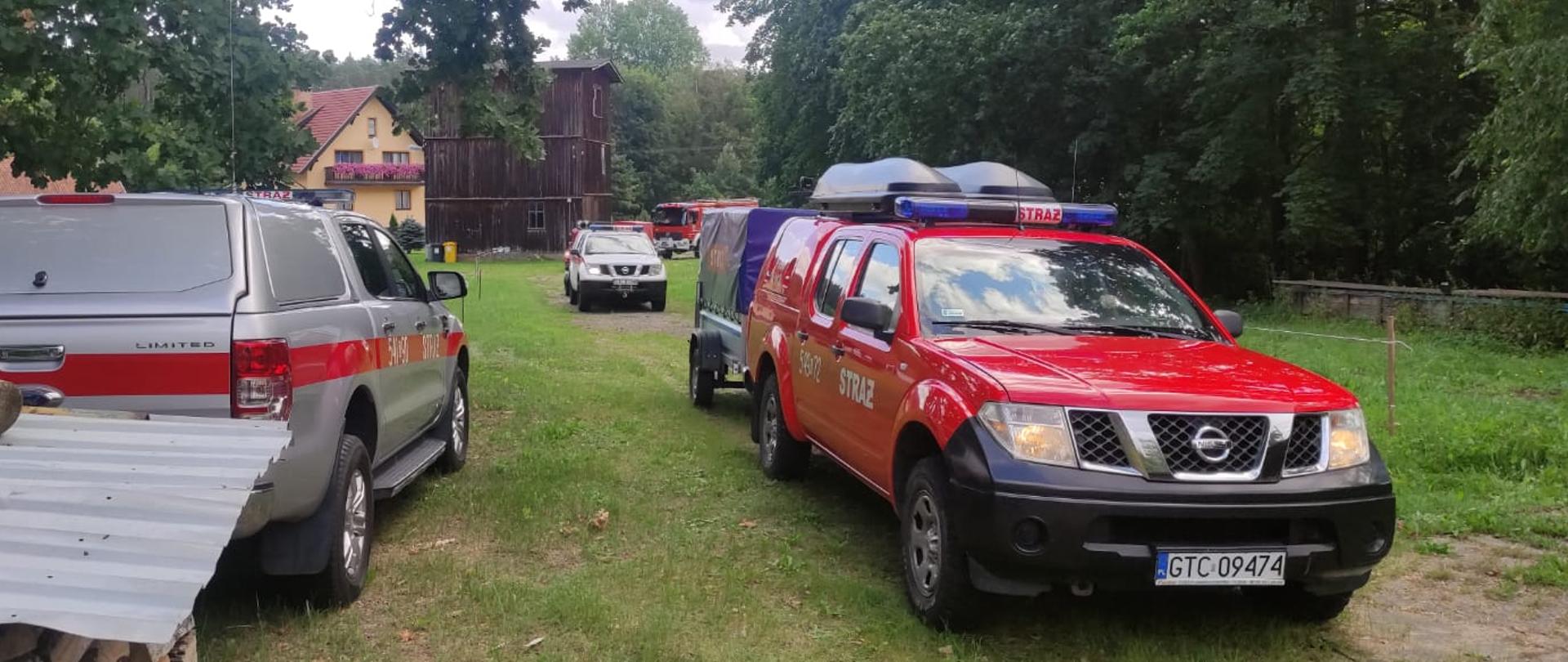 Trzy samochody rozpoznawczo-ratownicze na łące. Wkoło drzewa.