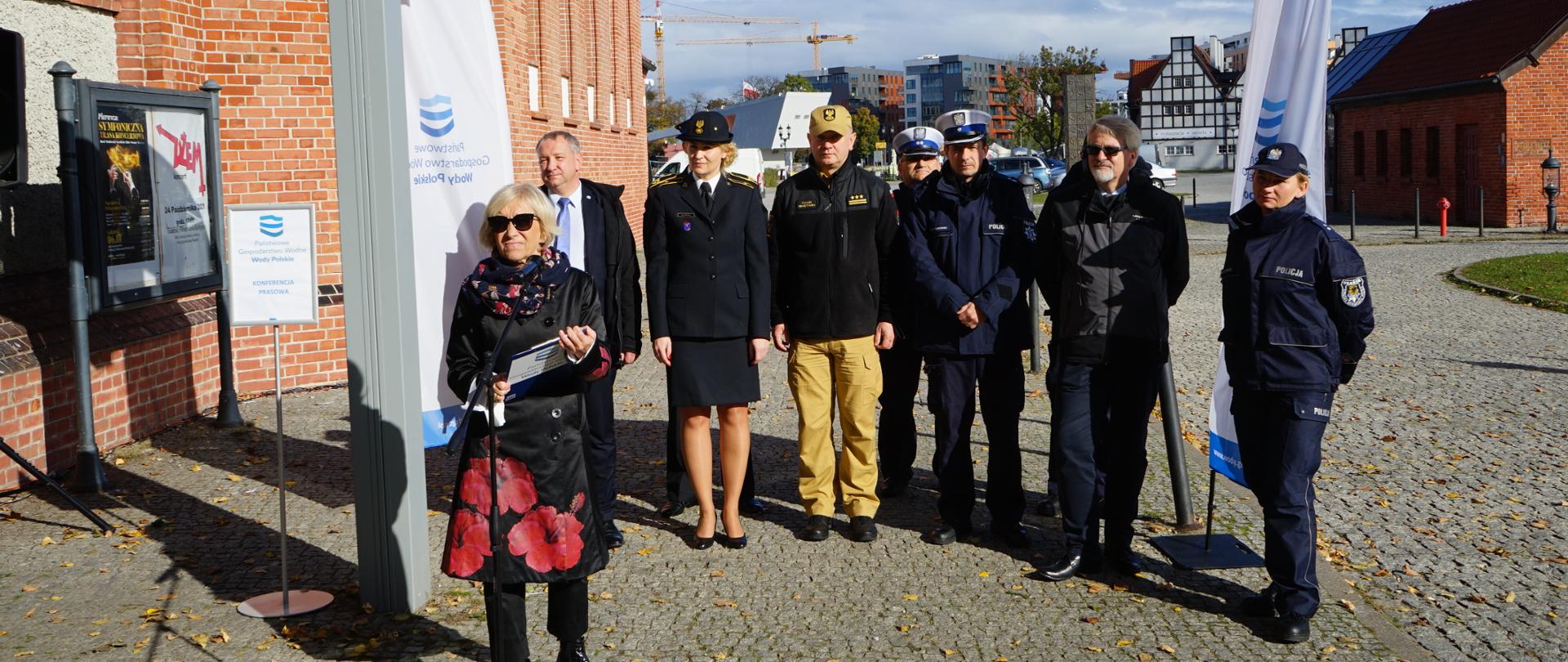 Kobieta przemawia do mikrofonu, za nią stoją zaproszeni goście oraz partnerzy programu.