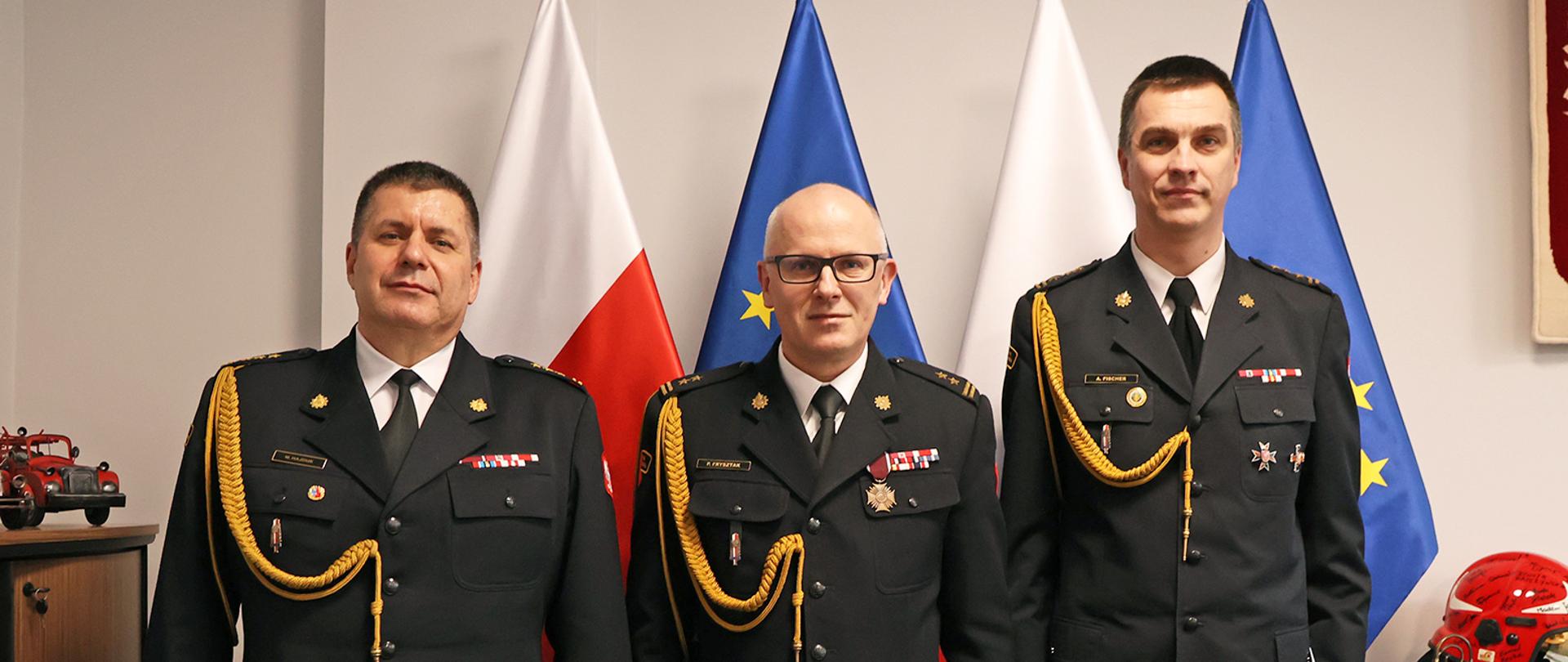 Strażacy podczas wręczania decyzji w pomieszczeniu na tle flag.