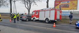 Zdjęcie przedstawia samochód osobowy oraz wóz strażacki po kolizji drogowej, strażaków PSP i OSP oraz Policjantów podczas prowadzenia działań.