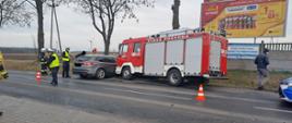 Zdjęcie przedstawia samochód osobowy oraz wóz strażacki po kolizji drogowej, strażaków PSP i OSP oraz Policjantów podczas prowadzenia działań.