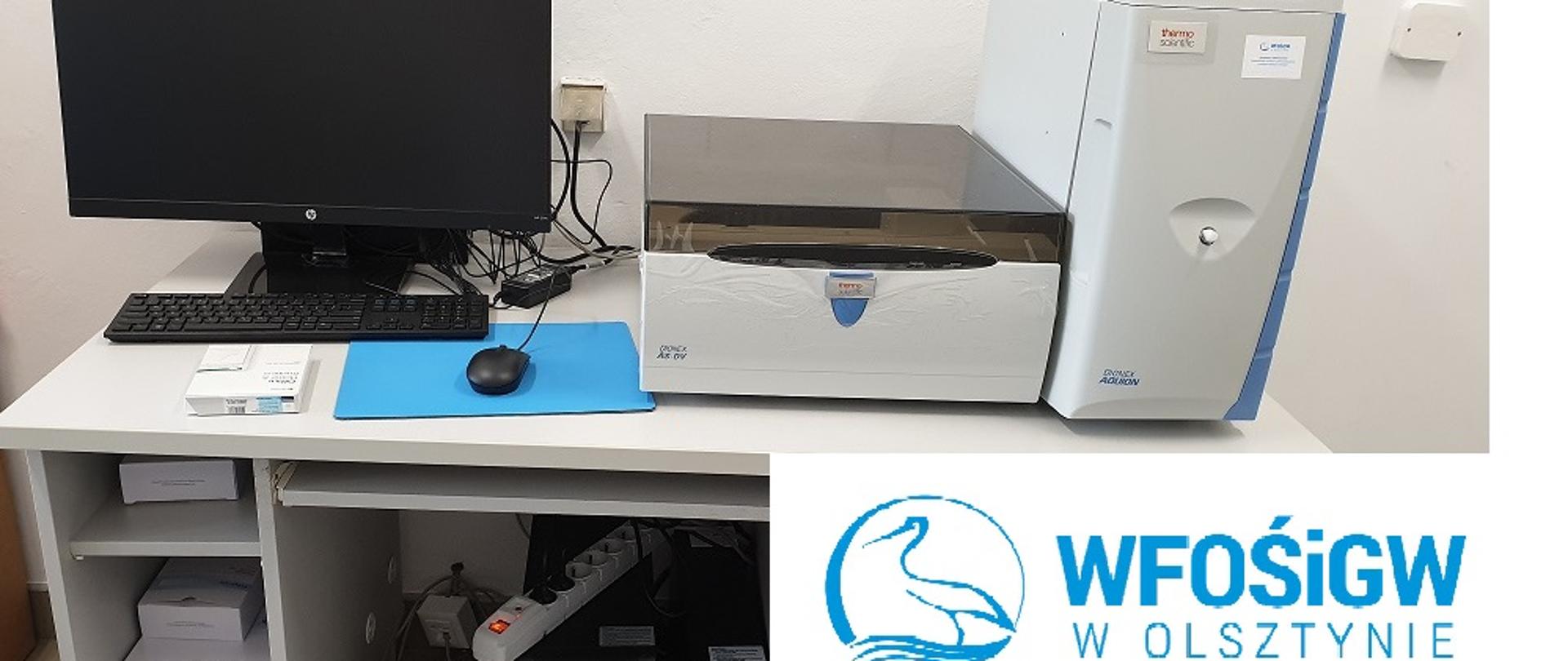 Chromatograf jonowy stojący na biurku w laboratorium, a także komputer z monitorem oraz logo WFOŚiGW 