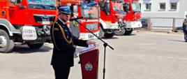 W Zambrowie odbyła się uroczystość z okazji Powiatowych Obchodów Dnia Strażaka. zastępca podlaskiego komendanta wojewódzkiego Państwowej Straży Pożarnej - mł. bryg. Łukasz Chankowski przemawia przy mównicy, w tle wozy strażackie i dowódca uroczystości