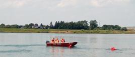 Zdjęcie ukazuję pięciu ratowników. Dwóch z nich znajduję się wodzie i ćwiczy określone założenie natomiast trzech pozostałych obserwuje ćwiczenia z łodzi. 