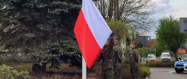 Żołnierze podnoszą uroczyście flagę państwową na maszt.