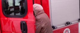 Na zdjęciu widać starszą kobietę która wsiada do pojazdu pożarniczego jednostki OSP Biskupice