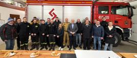 Grupa strażaków w garażu pozująca na tle pojazdu gaśniczego.