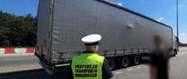 Na pierwszym planie: umundurowany inspektor wielkopolskiej Inspekcji Transportu Drogowego i kontrolowany kierowca litewskiej ciężarówki. W tle: ciągnik siodłowy z podpiętą naczepą. Ładunek opiera się o plandekę naczepy.