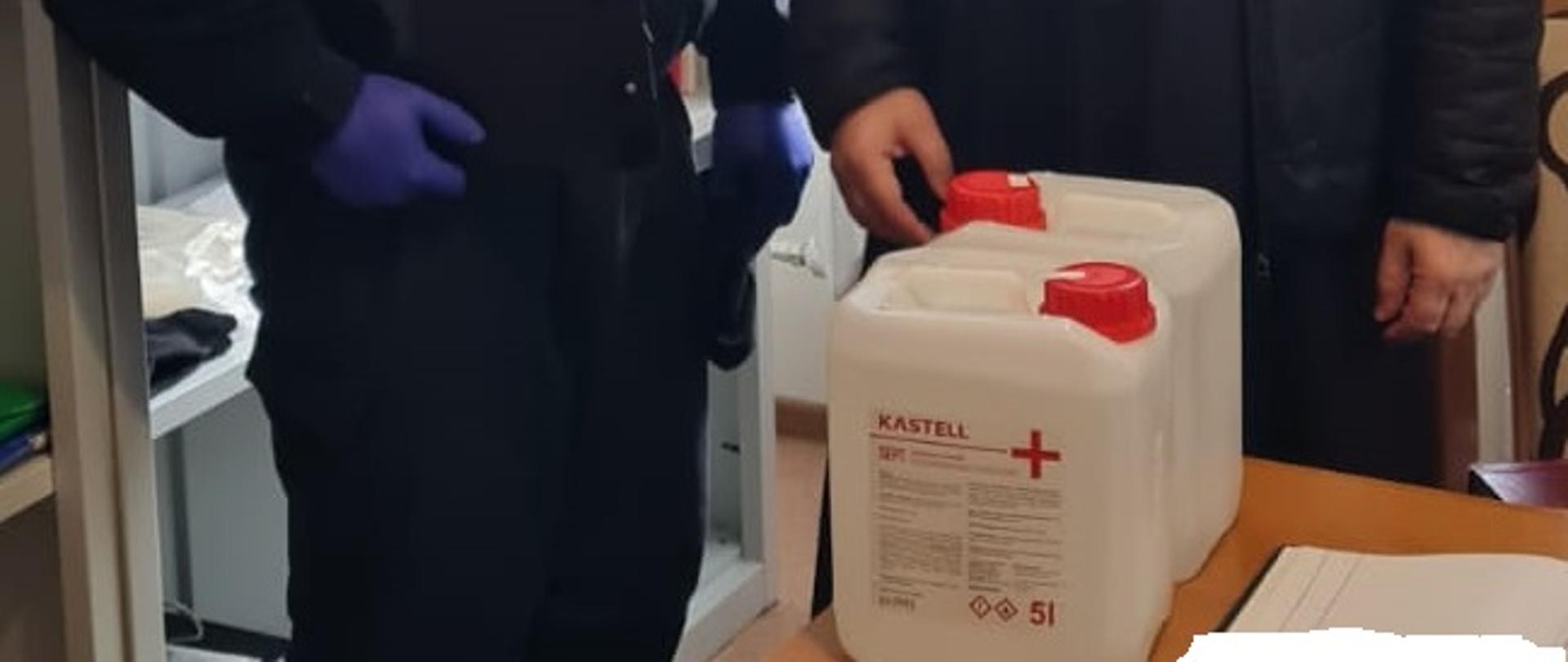 Zdjęcie obrazuje przekazanie księdzu przez strażaka płynu do dezynfekcji.