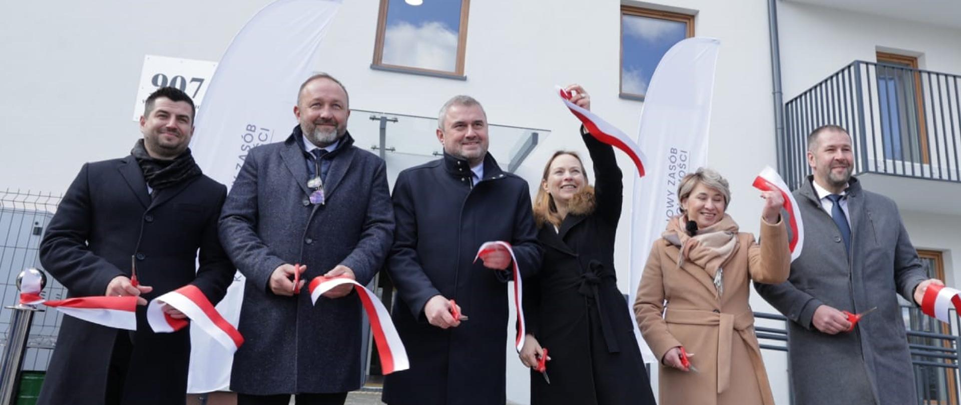 Sześć osób stoi przed blokiem z przeciętą biało-czerwoną wstęgą.