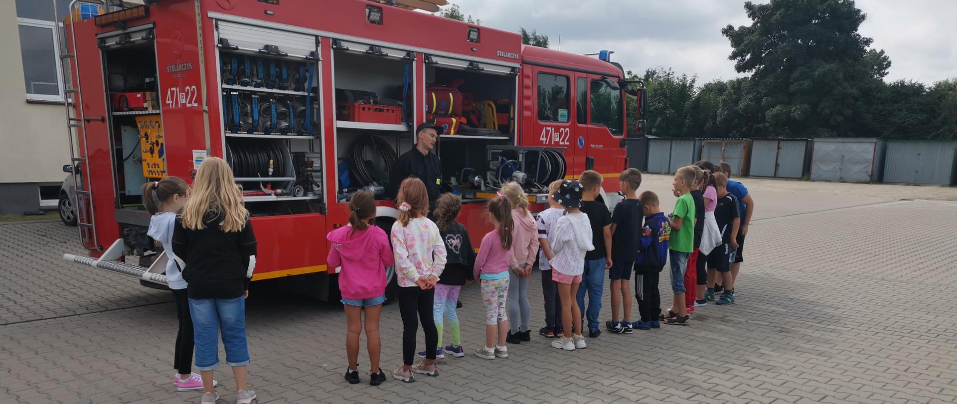 Zdjęcie przedstawia dzieci oraz strażaka prezentującego sprzęt pożarniczy.