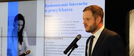 Wiceminister zdrowia Janusz Cieszyński przemawia do mikrofonu.