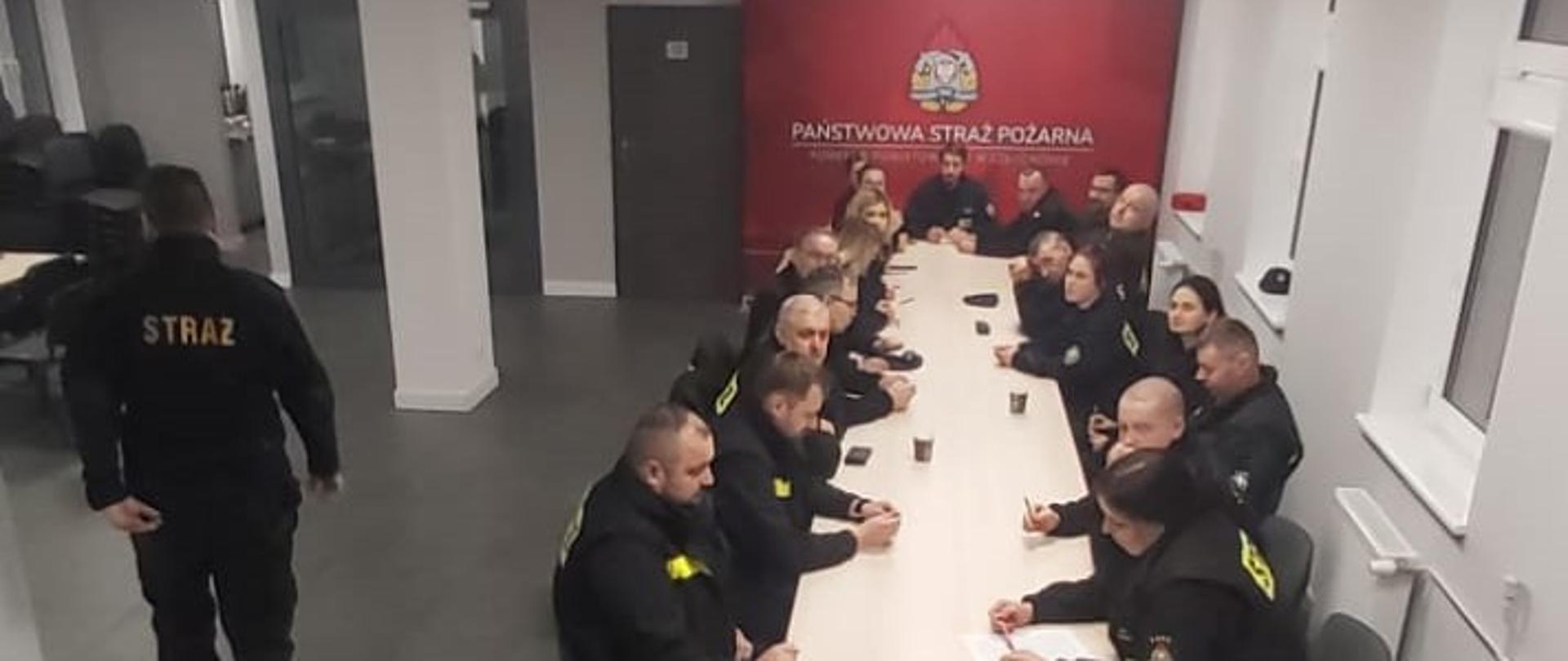 Druhny i druhowie siedzą przy stole na sali w Komendzie Powiatowej Państwowej Straży Pożarnej w Człuchowie. Przygotowanie do części teoretycznej egzaminu.