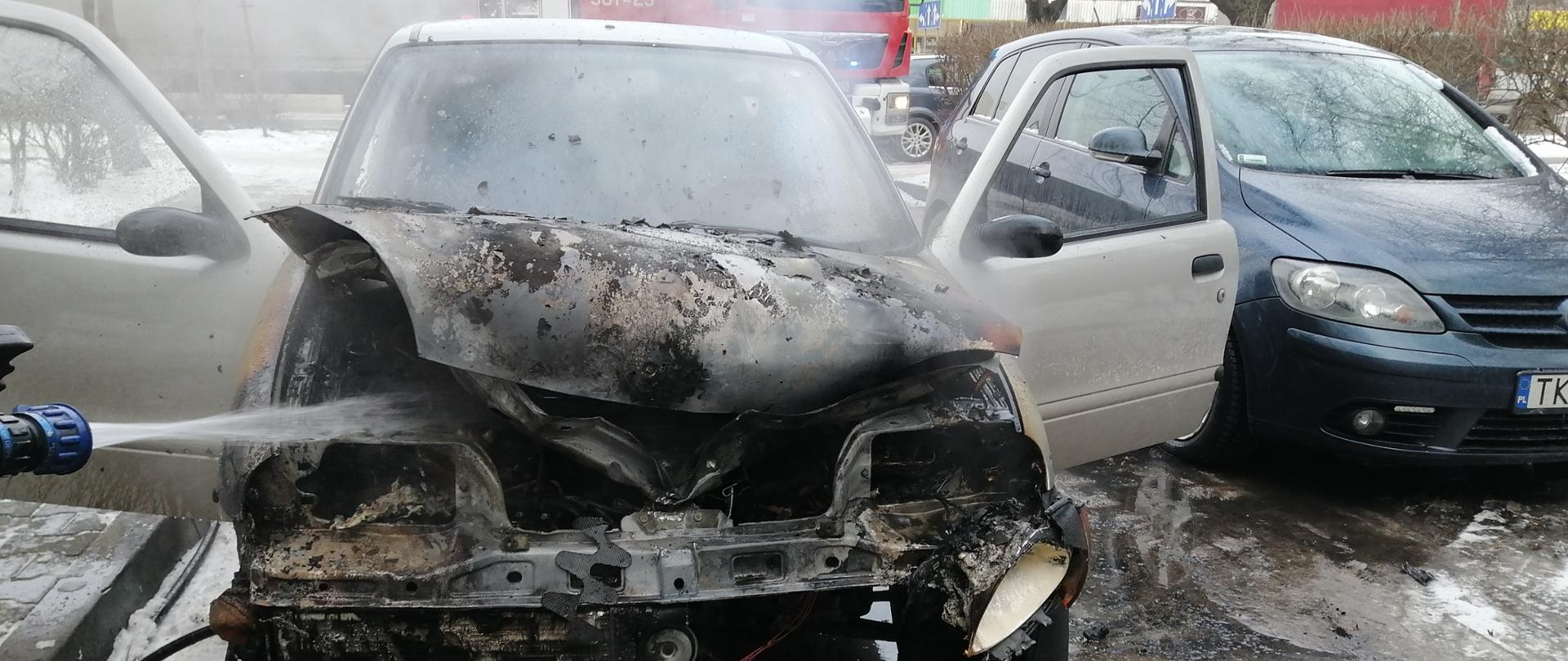 Na zdjęciu widzimy spalony samochód osobowy. Widać prąd wody podawany do komory silnika.