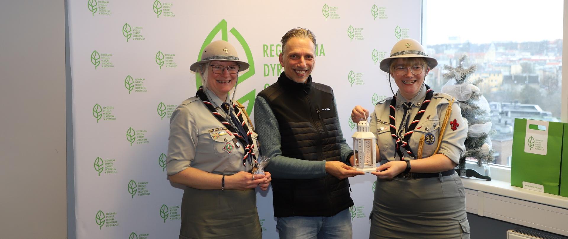 Dwie Harcerki a po środku stoi Zastępca Dyrektora RDOS w Bydgoszczy trzyma biały lampion