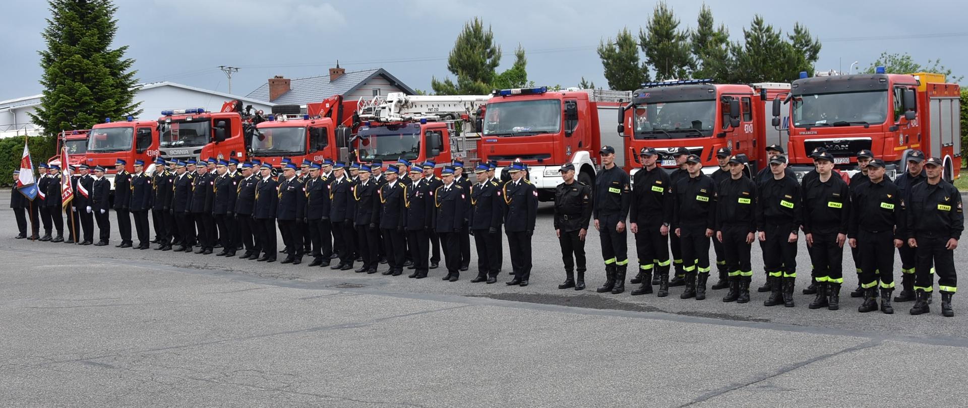 Na zdjęciu widać stojących na placu apelowym od lewej: dowódcę jednostki ratowniczo-gaśniczej, poczet sztandarowy komendy powiatowej państwowej straży pożarnej w Jarosławiu, poczet sztandarowy ochotniczych straży pożarnych i strażaków ustawionych w dwuszeregu. Strażacy ubrani są w umundurowanie wyjściowe lub koszarowe. Na drugim planie widoczne są pojazdy strażackie.