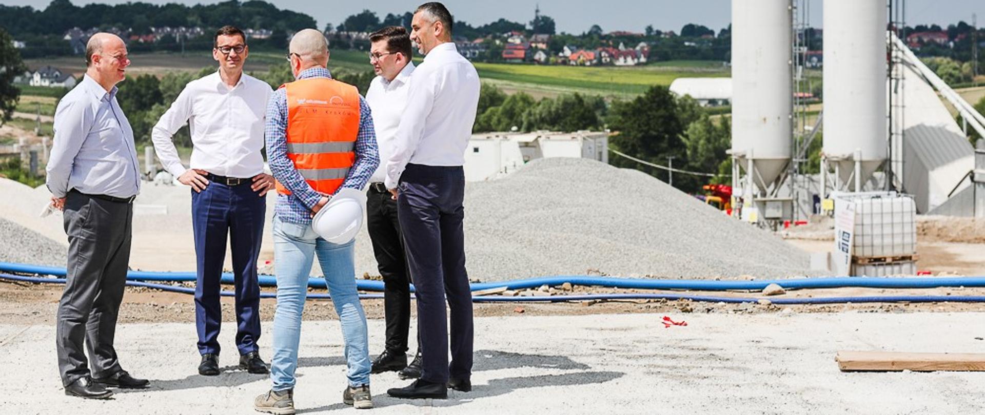 Premier, wojewoda oraz pozostali stoją na terenie budowy drogi.