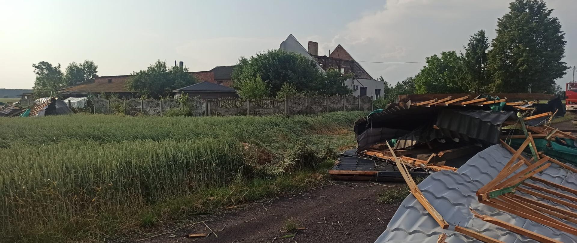 Zerwany dach, pogięta blacha, połamana więźba dachowa, w tle wozy strażackie.