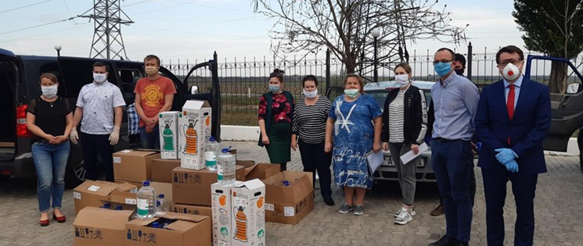 Grupa ludzi i paczek oraz butli plastikowych na parkingu samochodowym