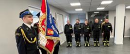Po lewej stronie stoi poczet sztandarowy w tle funkcjonariusze KP PSP w Człuchowie stojący w dwuszeregu podczas uroczystości składania ślubowania str. str. Grzegorza Hinz. 