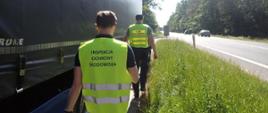 Pracownicy Inspekcji Ochrony Środowiska i Służby Celno-Skarbowej idą wzdłuż naczepy kontrolowanego pojazdu stojącego na parkingu przy drodze.