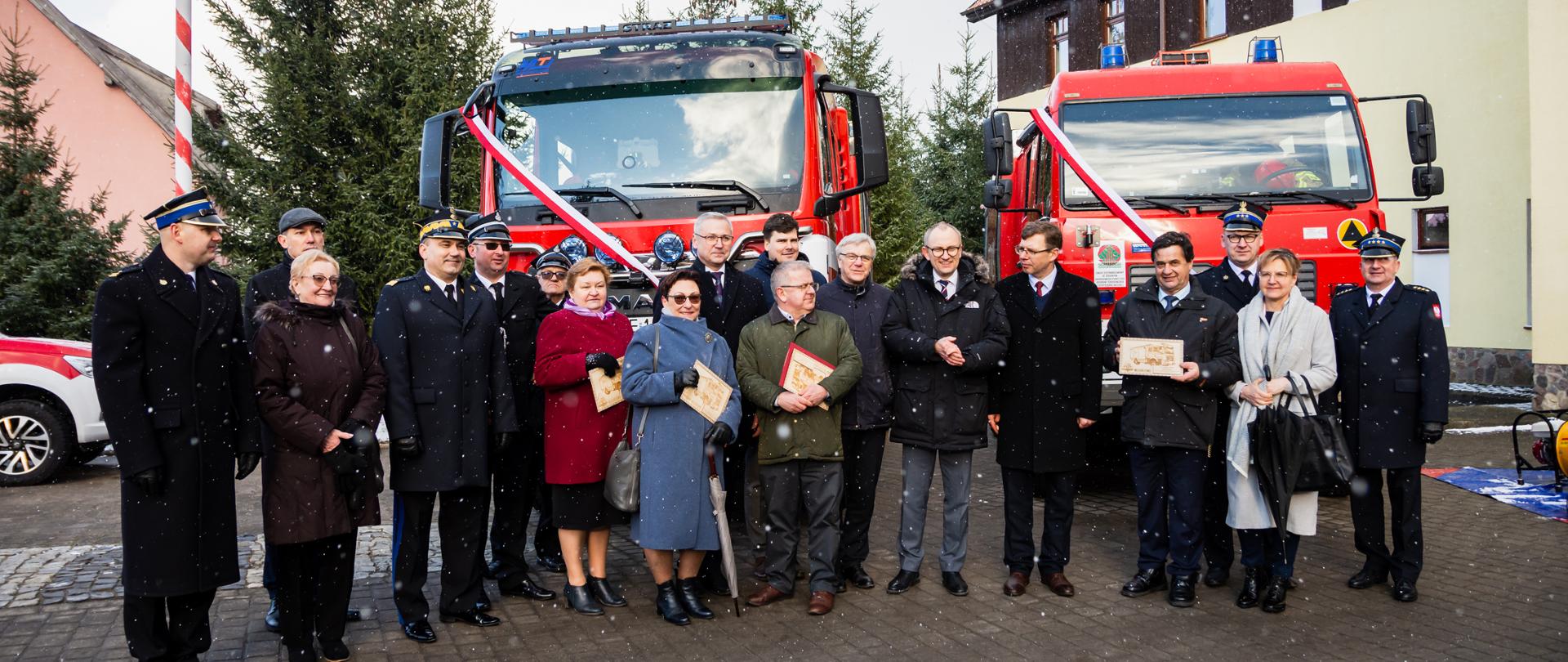 Zaproszeni goście stoją na placu KP za nimi widać dwa samochody, które zostały przekazane 