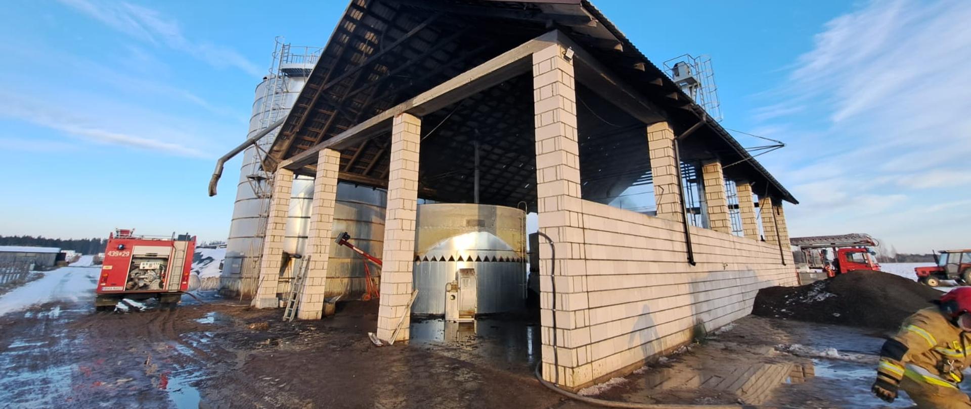 Murowana wiata, wewnątrz silos. Obok większy silos. Po lewej stronie wóz strażacki.