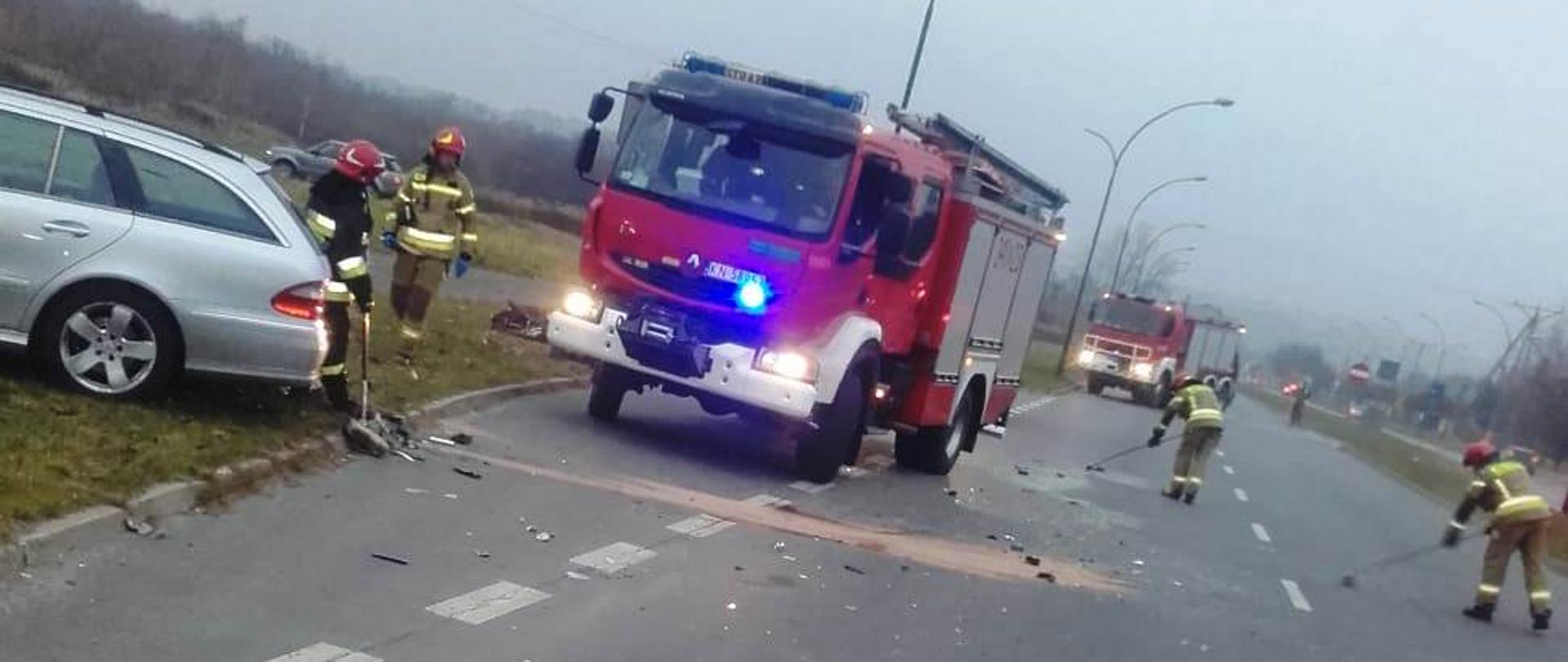 Samochód osobowy i pożarniczy na poboczu. Strażacy usuwają rozbite elementy. 