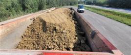 Na pierwszym planie: przestrzeń ładunkowa naczepy - wywrotki z przewożoną ziemią z wykopów. W tle: za kontrolowanym zespołem pojazdów stroi oznakowany furgon mazowieckiej Inspekcji Transportu Drogowego.