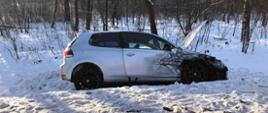 Na zdjęciu widoczny jest samochód osobowy Volkswagen Golf koloru srebrnego. Pojazd znajduje się w przydrożnym rowie. Samochód ma otwarta przednia maskę oraz widoczne uszkodzenia w postaci pogiętych przednich drzwi prawych oraz przedniego błotnika. Za pojazdem widoczne są drzewa. Przed pojazdem na śniegu widoczne są drobne elementy plastikowe z uszkodzonego pojazdu.