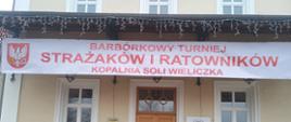 Zdjęcie przedstawia sześciu strażaków w umundurowaniu bojowym w nomeksach, czerwonych hełmach siedzących na schodach. W tle nad nimi wejście do Szybu Daniłowicza oraz napis nad nimi " Barbórkowy Turniej Strażaków i Ratowników Kopalnia Soli Wieliczka"