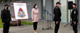 Zdjęcie zrobione na tle Jednostki Ratowniczo-Gaśniczej nr 3 w Rzeszowie. Po prawej stronie nadbrygadier Andrzej Babiec przyjmuje meldunek od dowódcy uroczystości. Na środku zdjęcia stoi wojewoda podkarpacki Ewa Leniart. Za nią tablica z logo Komendy Miejskiej Państwowej Straży Pożarnej w Rzeszowie. Po lewej stronie zdjęcia stoi komendant miejski Państwowej Straży Pożarnej w Rzeszowie. Strażacy ubrani są w mundury dowódczo sztabowe.