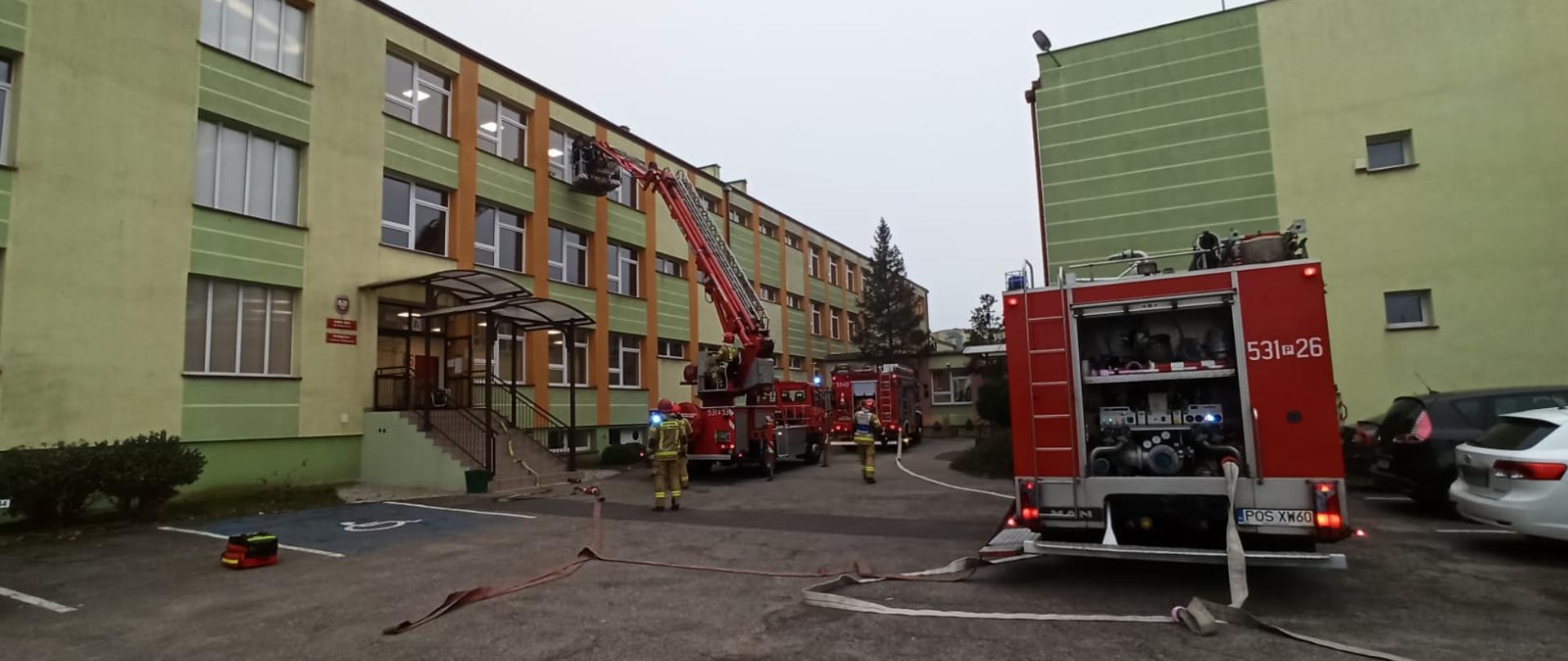 Strażacy ewakuują uczniów z okna budynku szkoły przy pomocy podnośnika.