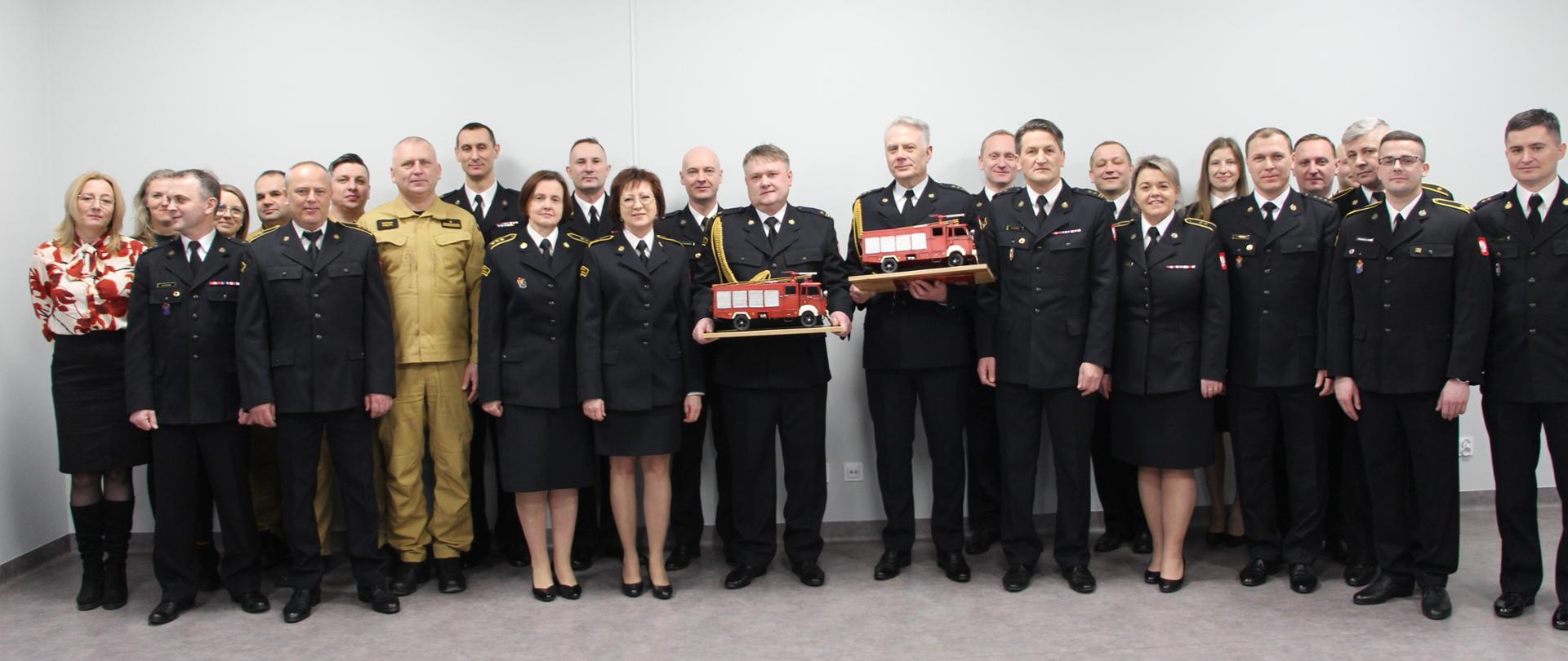 Pamiątkowe zdjęcie: funkcjonariusze i pracownicy Komendy Miejskiej Państwowej Straży Pożarnej w Kielcach. W pierwszym rzędzie stoją w centralnym punkcie odchodzący na emeryturę strażacy.
