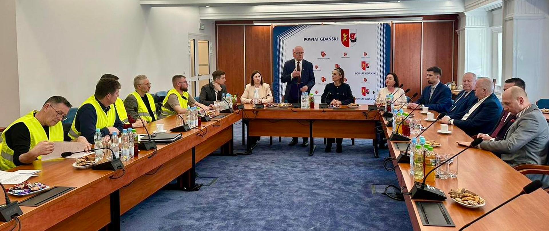 sala, wielki stół, siedzi kilkanaście osób, cześć to rolnicy z żółtych kamizelkach, 