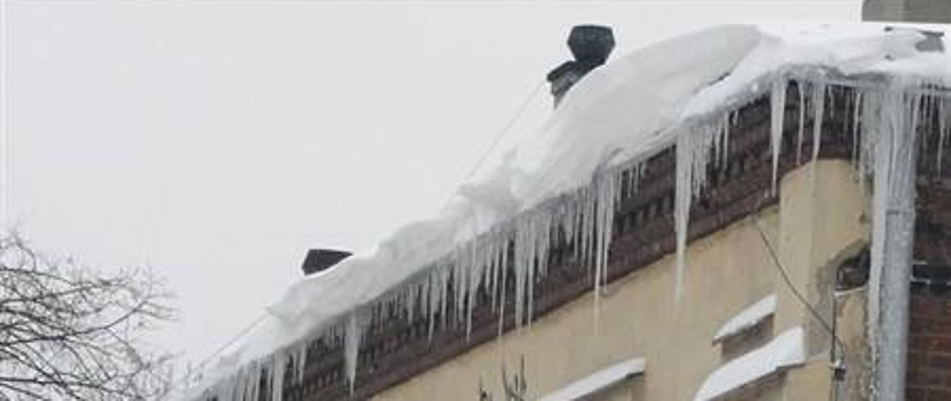 Nawisy śniegu i lodu widoczne na dachu budynku. Przypomnienie, że obowiązek odśnieżania dachów i usuwania nawisów śniegu i lodu, spoczywa na właścicielach, zarządcach i administratorach obiektów.