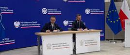 Za stolikiem siedzą minister Kulasek i minister Kosiniak-Kamysz, podpisują dokumenty, za nimi granatowa ścianka z napisem Ministerstwo Nauki i Szkolnictwa Wyższego i Ministerstwo Obrony Narodowej, z prawej pod ścianą flagi Polski i UE.