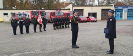 Zdjęcie przedstawia złożenie meldunku Komendantowi Powiatowemu PSP w Brodnicy st. bryg. Andrzejowi Góreckiemu. W tle strażacy PSP w Brodnicy oraz samochody Komendy Powiatowej.